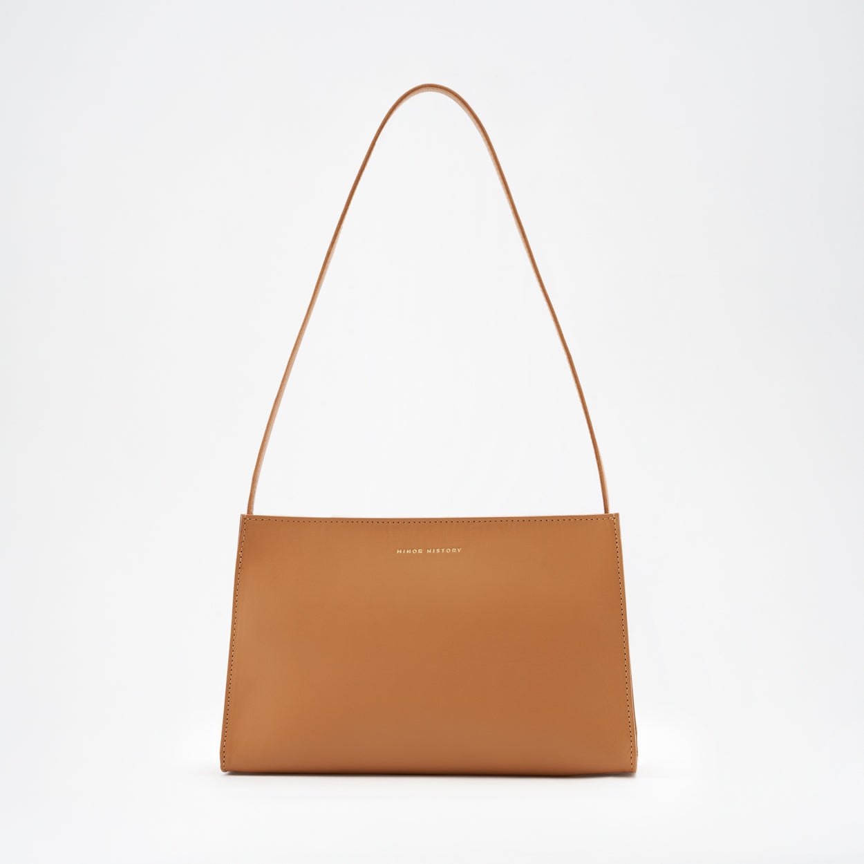 A brown leather shoulder bag with a minimal design, a sturdy zipper, and a delicate shoulder strap, displayed against a white background. - Saddle
