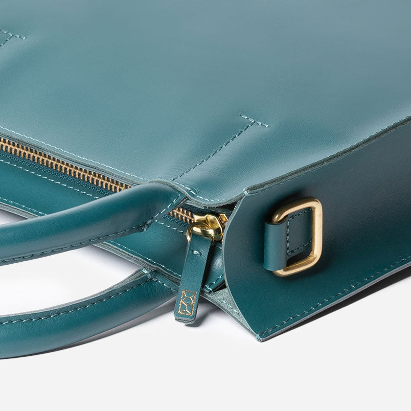 Close-up of a teal handbag with gold zipper and buckle on a white  - Dawnbackground