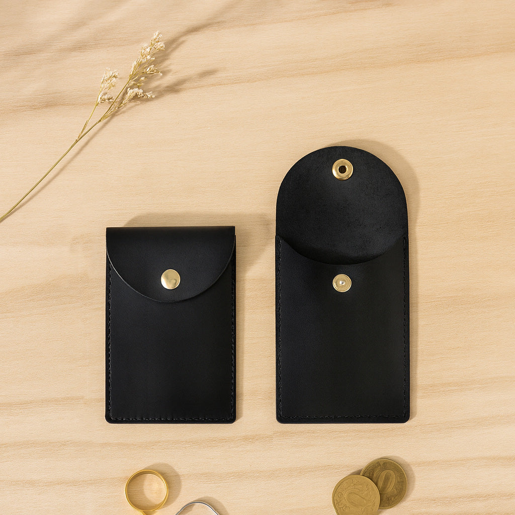Two black leather pouches with gold buttons on a wooden surface. - Black