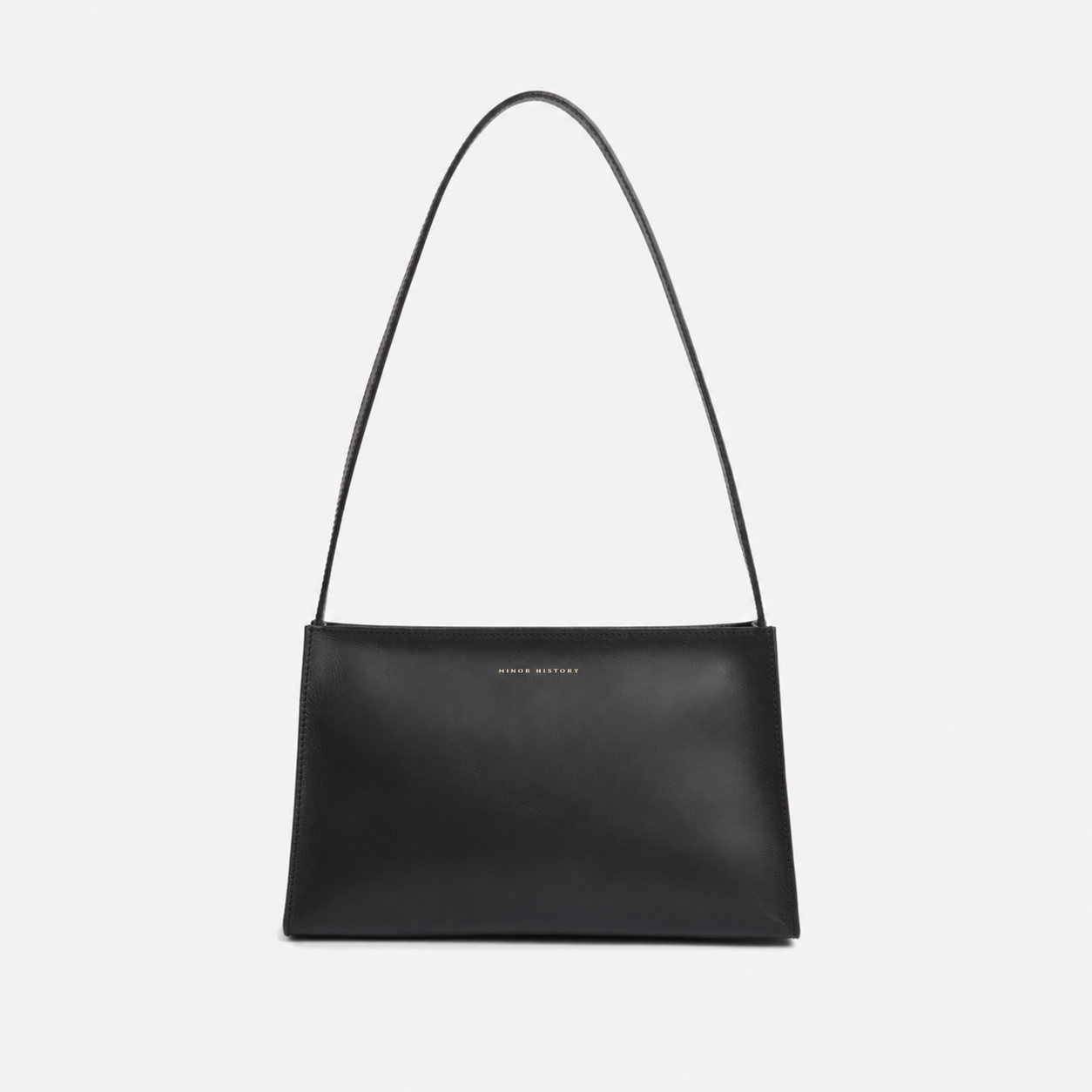 A brown leather shoulder bag with a minimal design, a sturdy zipper, and a delicate shoulder strap, displayed against a white background. - Saddle