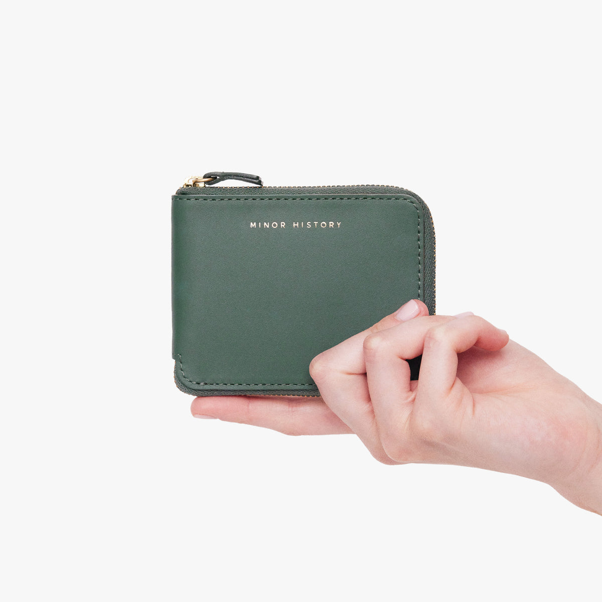A hand holding a green leather wallet with a zipper closure. - Evergreen
