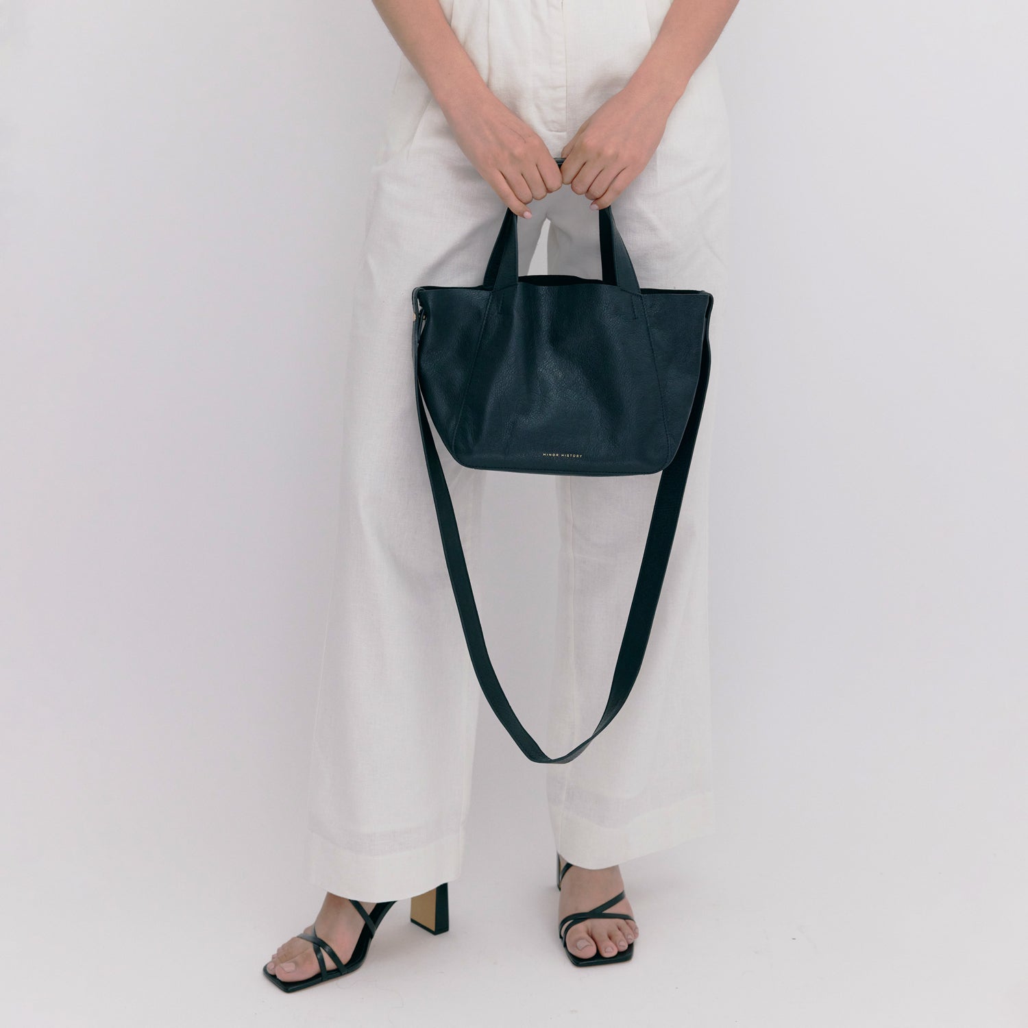 Person holding a black leather handbag against a white background - Black