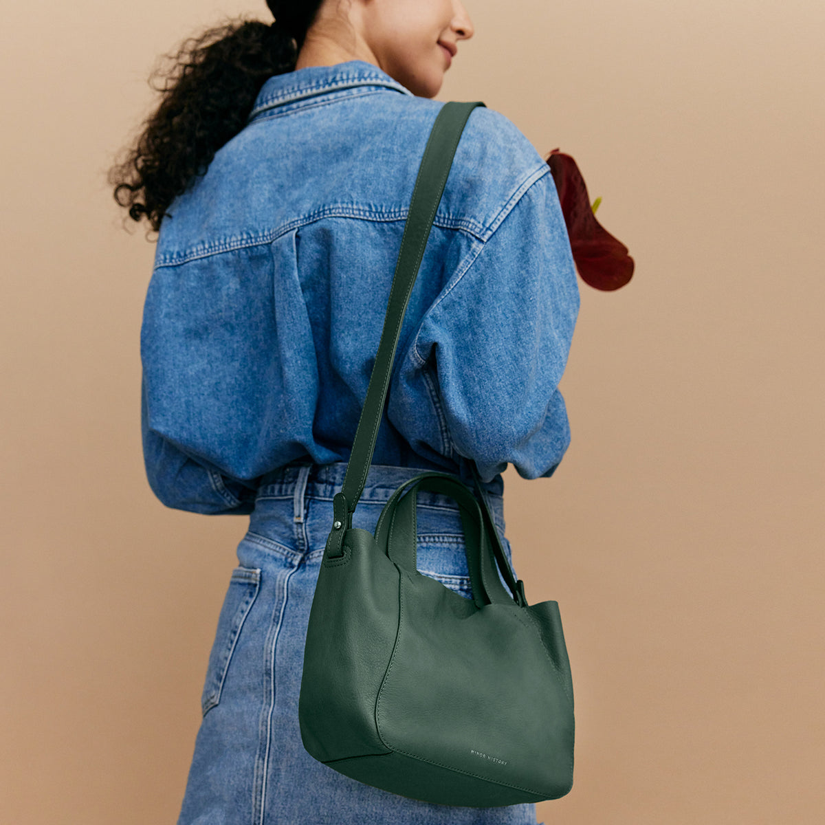 Person wearing a green handbag over their shoulder against a beige background - Evergreen