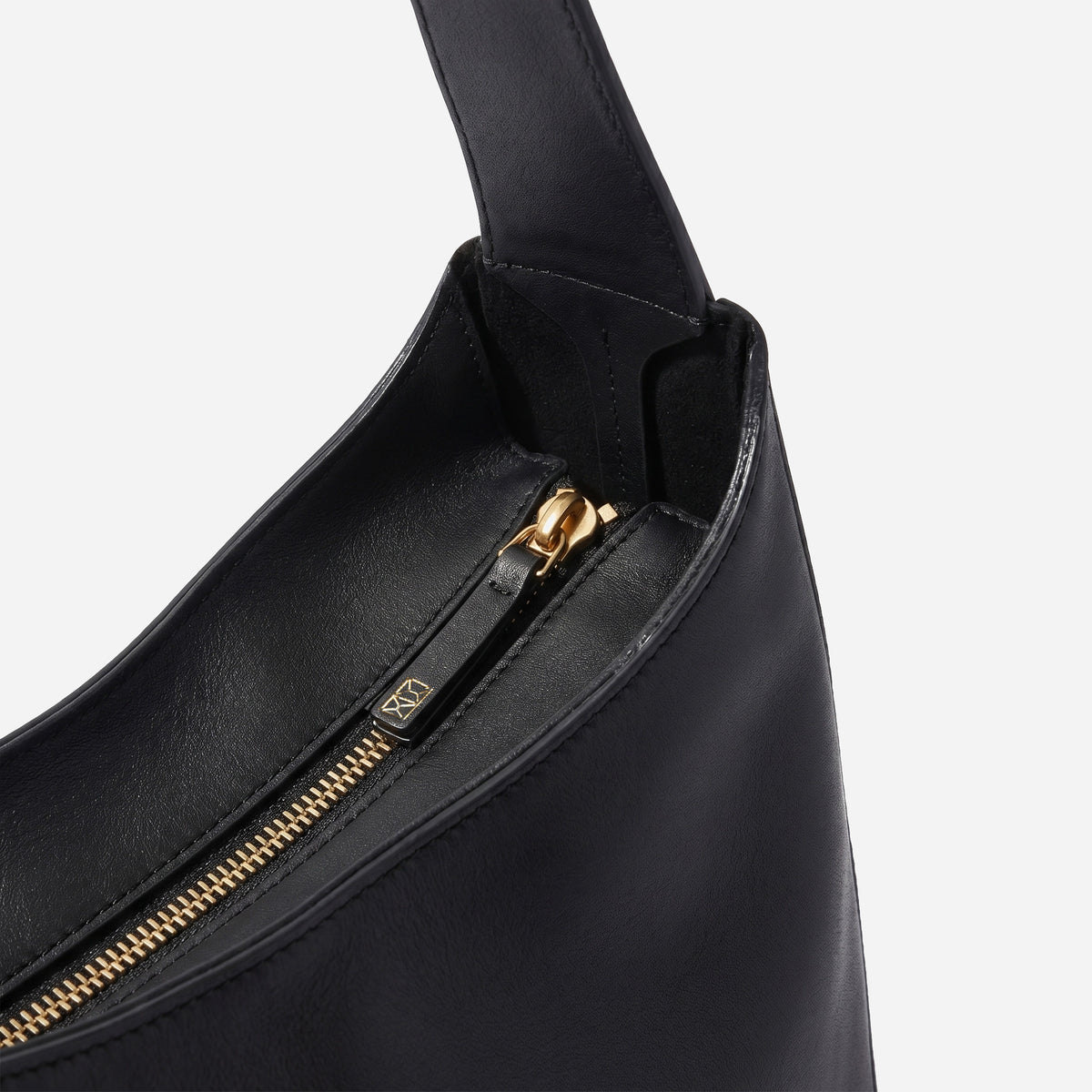 Black handbag with gold zipper on a light gray background -Black