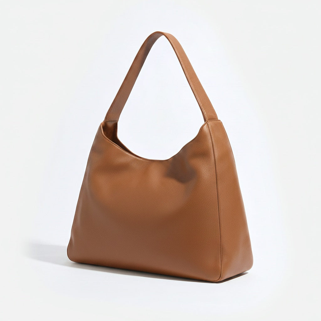 A medium brown pebbled leather hobo shoulder bag with a single strap, shown from a three-quarter angle on a clean white background.  -Saddle