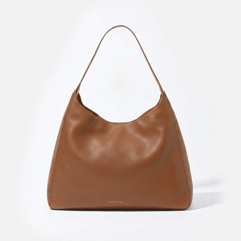 A brown pebbled leather hobo shoulder bag with a single thin strap, photographed against a clean white background. - Saddle