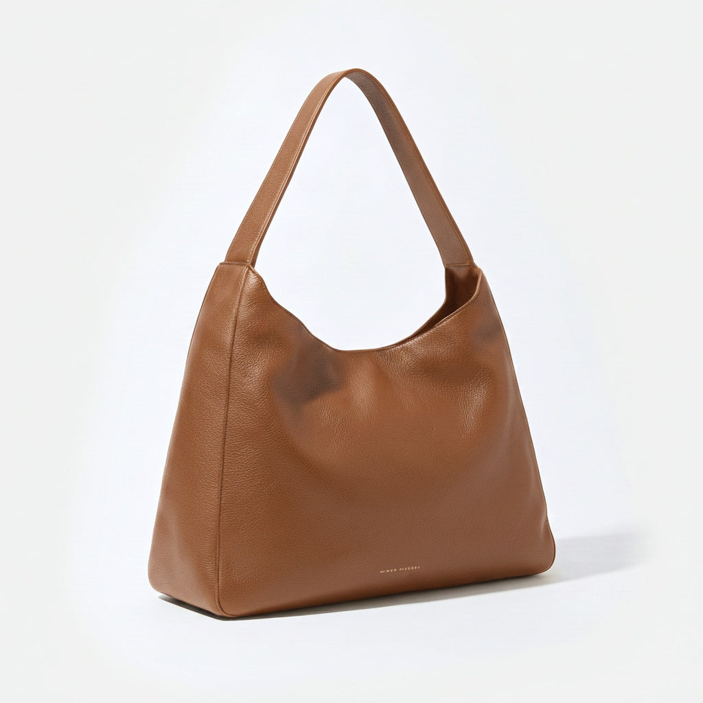 A medium brown pebbled leather hobo shoulder bag with a single strap, shown from a three-quarter angle on a clean white background. - Saddle
