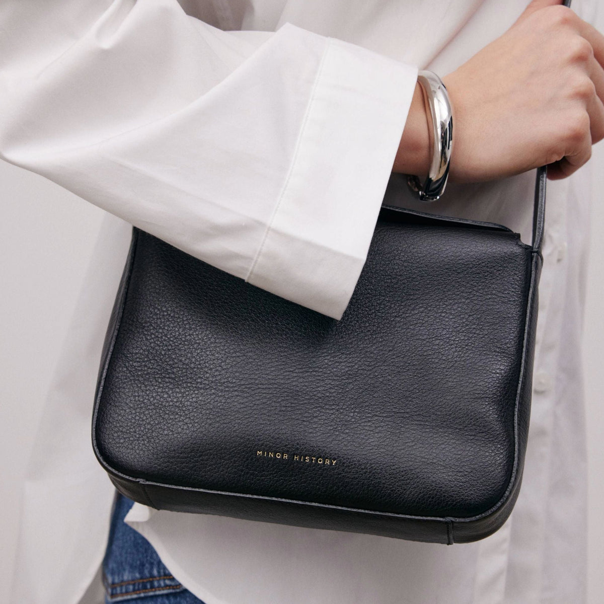 Little Frame crossbody bag in black full-grain leather carried by hand with tailored trousers for a polished style, minimalist women's handbag - Black