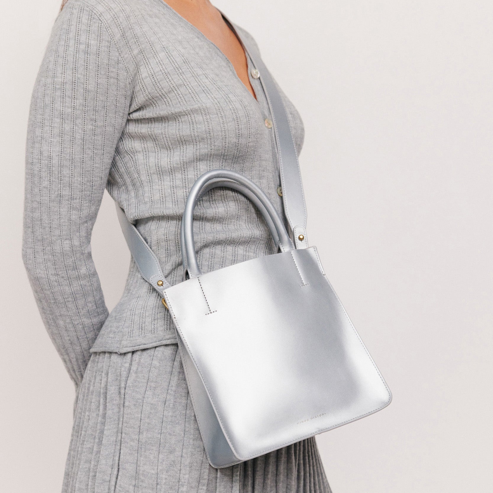 A silver crossbody leather bag with a removable strap and brass hardware, displayed against a plain background. - Sterling