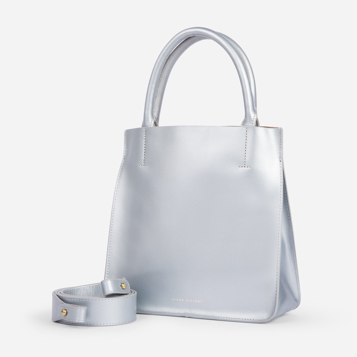 A silver crossbody leather bag with a removable strap and brass hardware, displayed against a plain background. - Sterling