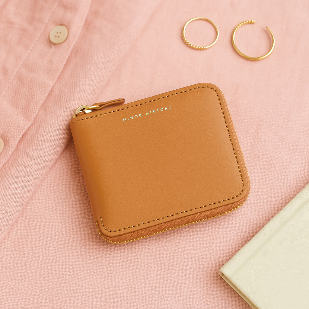 Brown wallet with 'Minor History' branding on a pink fabric background - Saddle