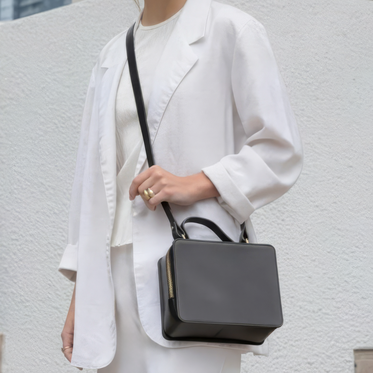 Woman in a white outfit holding a black handbag against an urban background - Black