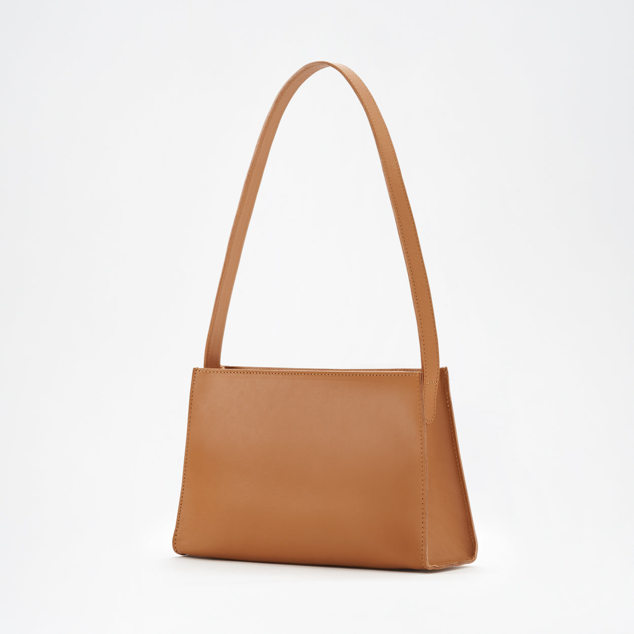 A brown leather shoulder bag with a minimal design, a sturdy zipper, and a delicate shoulder strap, displayed against a white background. - Saddle